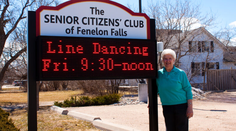 Senior standing by club sign